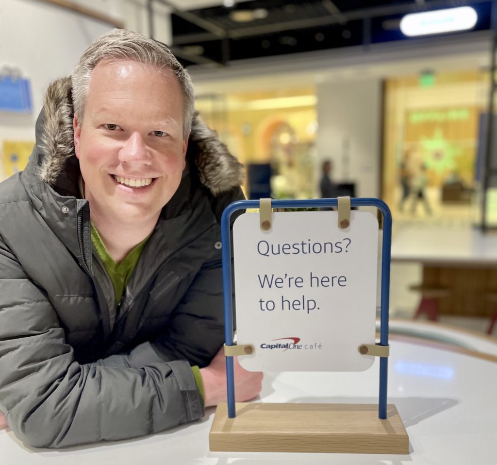 Aaron Hurd in front of a sign that says "We're here to help." at the Capital One Cafe at the Mall of America.